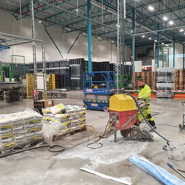 Arbeider i et lagerlokale med gulvavretting og sekker med materialer i bakgrunnen